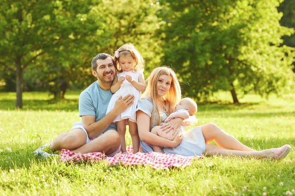 Lycklig familj sitter på det gröna gräset leker i parken. — Stockfoto