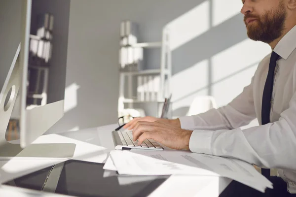 Travailler en ligne. Un homme d'affaires sérieux et occupé lit des documents de travail assis à une table avec un ordinateur dans le bureau. — Photo