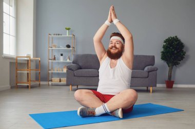 Nilüfer pozisyonunda meditasyon yapan şişman bir adam evde yerde oturuyor.