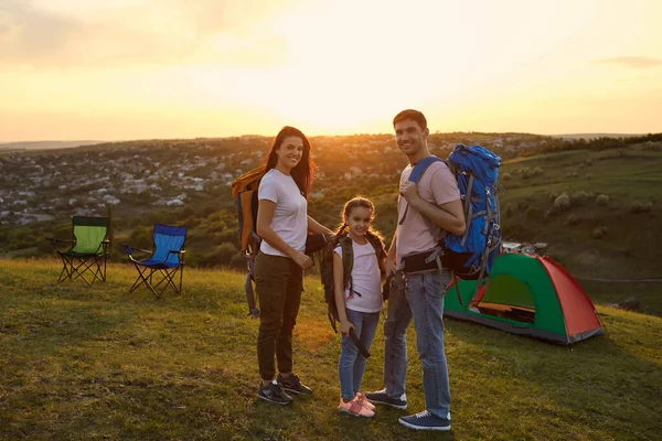 Rodina na táboření v přírodě. Portrét šťastné rodiny s batohy stojící u stanu na hoře při západu slunce. — Stock fotografie