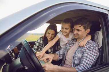 Yolculuk sırasında araba kuaföründe haritaya bakan mutlu genç bir aile. Kızı olan sevgi dolu ebeveynler otomobille seyahat ediyorlar.