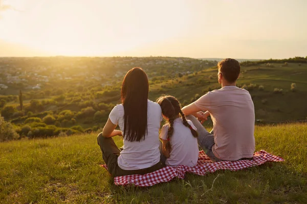 Widok z tyłu młodej rodziny z dzieckiem siedzi na kocu piknikowym i patrząc na piękny zachód słońca w górach, przestrzeń kopiowania — Zdjęcie stockowe