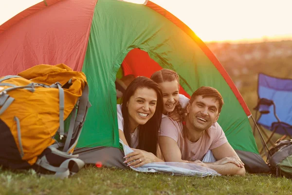 Счастливая семья с ребенком на кемпинге, расслабляясь в палатке. Заботливые родители и их дочь отдыхают в лагере — стоковое фото