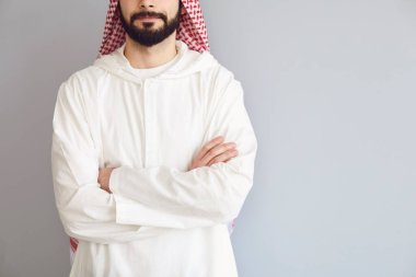 Kendine güveni olan Arap bir adam gri bir arka planda kollarını kavuşturdu.