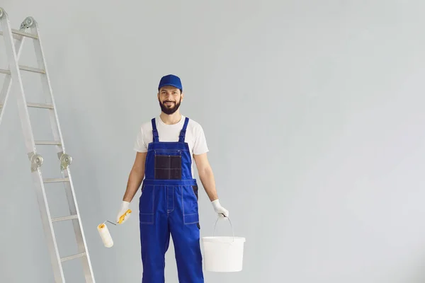 Trabalhador pintor segurando escova de rolo e balde com tinta. — Fotografia de Stock