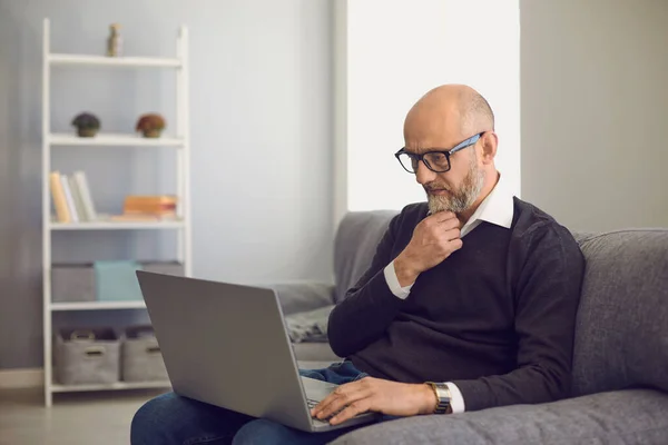 Senior man with laptop communicating online, working, consulting doctor or taking educational course in home — Zdjęcie stockowe