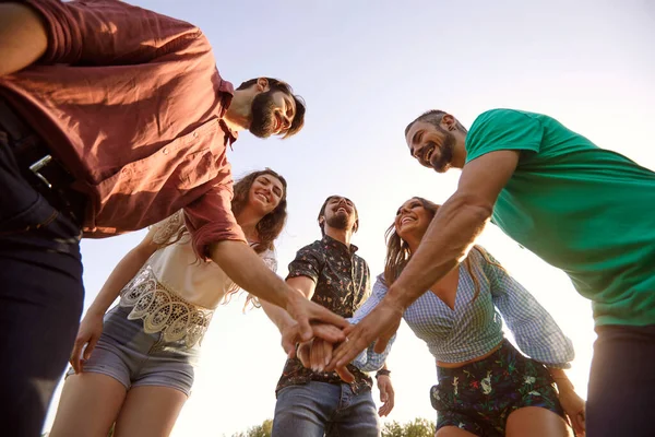 Laag gezichtspunt van jonge lachende vrienden die hun handen in een cirkel, buiten, bij elkaar leggen. Eenheids- of steunconcept — Stockfoto