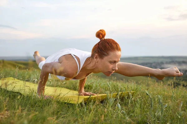 Yoga girl in nature. Woman is practicing yoga balance while standing in a pose on the grass on the nature in the summer outdoors.