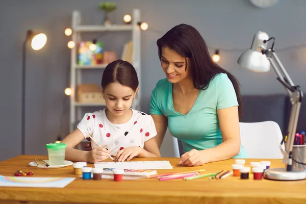 Kreativität und Entwicklung des Kindes. Glückliche Familienmutter und Tochter malen zu Hause am Tisch. — Stockfoto