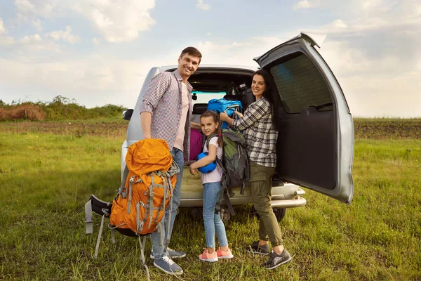 Щасливі батьки і дочка мандрівники беруть рюкзаки з машини для піших прогулянок на природі . — стокове фото