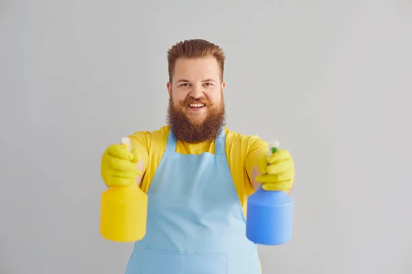 Hombre gordo divertido con barba en un delantal lavado limpia sobre un fondo gris. — Foto de Stock