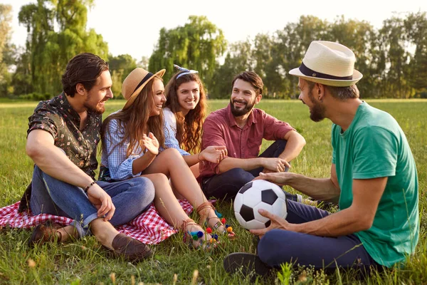 Group of friends having break after playing soccer outdoors. Young people communicating in countryside on summer day — Stock Photo, Image