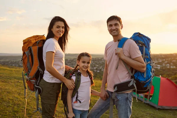 Молодая семья из трех человек с рюкзаками в горах. Счастливые родители и дочь наслаждаются летней туристической поездкой — стоковое фото