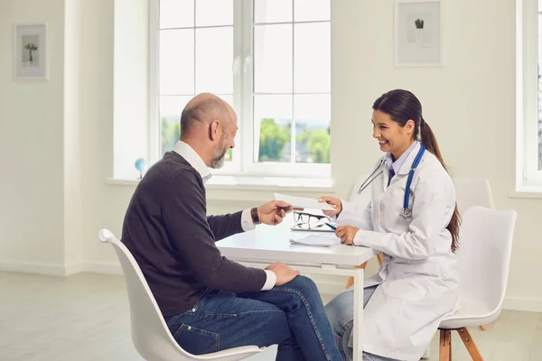 La doctora y el paciente están sentados en una mesa en el consultorio de una clínica médica . — Foto de Stock