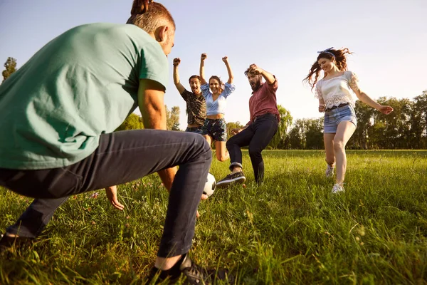 Amigos felizes a jogar futebol no prado verde. Grupo de estudantes universitários se divertindo, desfrutando de jogo de esportes ao ar livre — Fotografia de Stock