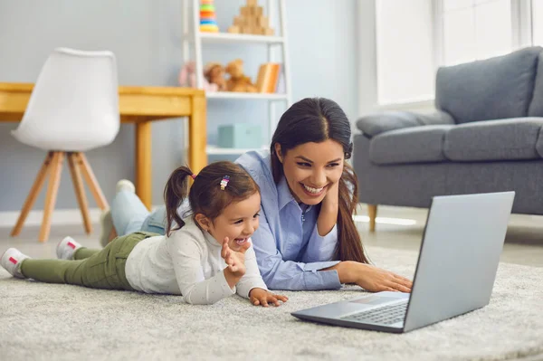 Мама с дочерью смотрят мультфильмы или развлекательное видео онлайн дома. Родитель и ребенок с ноутбуком на полу — стоковое фото