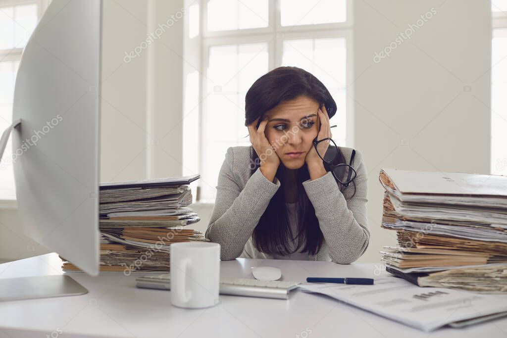 Woman brunette accountant in glasses with a mountain of documents on the table tired depressed emaciated disappointed depressive at the table in the office