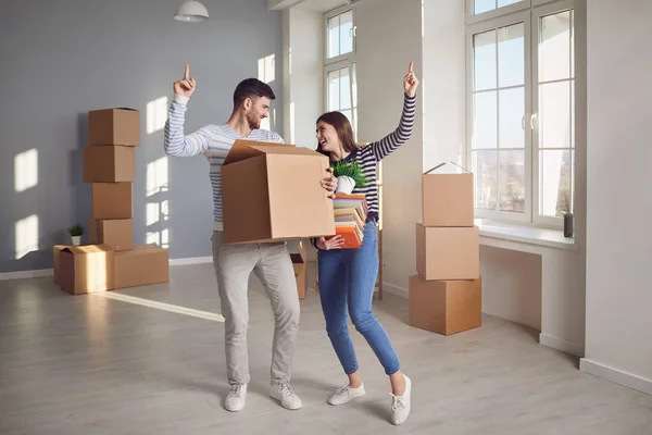 Ein fröhliches Paar spielt mit einer Umzugskiste in einem hellen Raum eines neuen Hauses. — Stockfoto