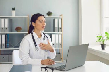 Çevrimiçi tıbbi danışmanlık. Kadın doktor klinikte dizüstü bilgisayarla hastayla konuşuyor. Sıhhiye, istemciyle video görüşmesi yapıyor