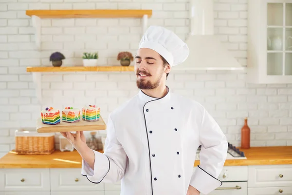 Cukrář muž se usmívá, zatímco stojí s dort v ruce v kuchyni pekárny — Stock fotografie