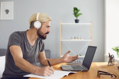 Evde ya da çevrimiçi eğitimde çalışmak. Kulaklık takmış çekici bir işadamı iş yerinde dizüstü bilgisayarla konferans yapıyor.