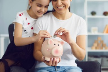 Aile finansmanı tasarruf kavramı. Arkadaş ve çocuk, evdeki sandalyede oturan domuz kumbarasına para yatırdılar.