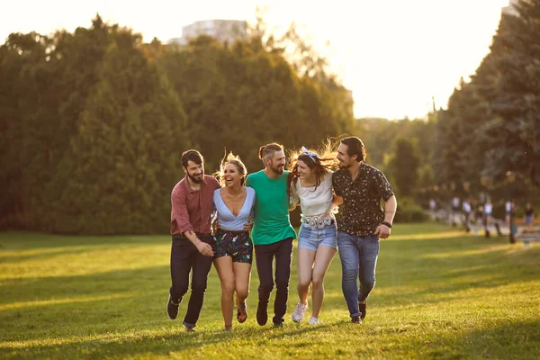 Группа молодых людей развлекается, обнимаясь на траве в летнем парке . — стоковое фото