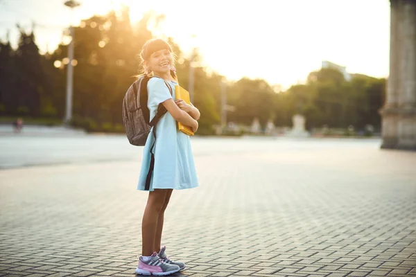 Une écolière avec un sac à dos et des livres se tient dans une rue de la ville. Retour à l'école . — Photo