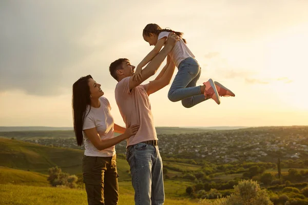 Joven familia alegre divirtiéndose con su hija en las montañas al atardecer. Padre criando a su hijo en el campo — Foto de Stock