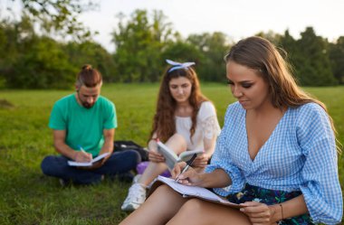 Kitapları ve defterleri olan bir grup genç üniversite öğrencisi parkta birlikte okuyorlar. Dışarıda ödev yapan arkadaşlar.