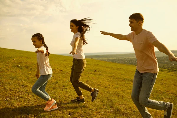 Familia alegre con mamá, papá y un niño pequeño corriendo en las montañas. Los padres con el niño se divierten jugando avión juego — Foto de Stock