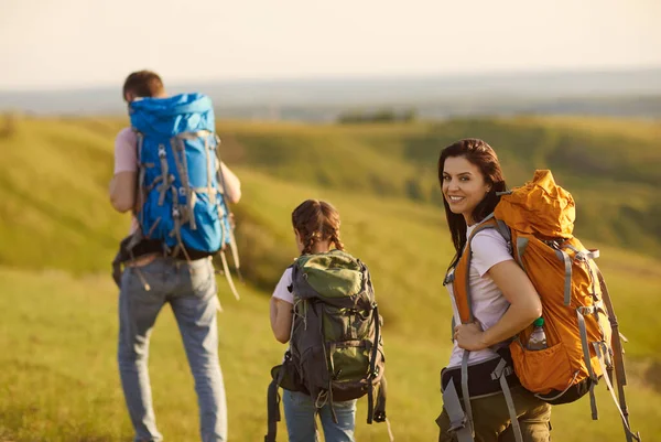 Familia de viajeros con mochilas caminan a lo largo de la hierba en las montañas en la naturaleza en verano . —  Fotos de Stock