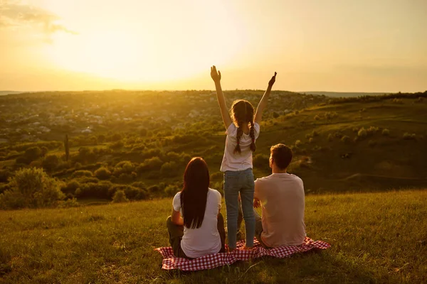 Visão traseira de uma família feliz descansando olhando para um belo pôr do sol à noite na natureza . — Fotografia de Stock