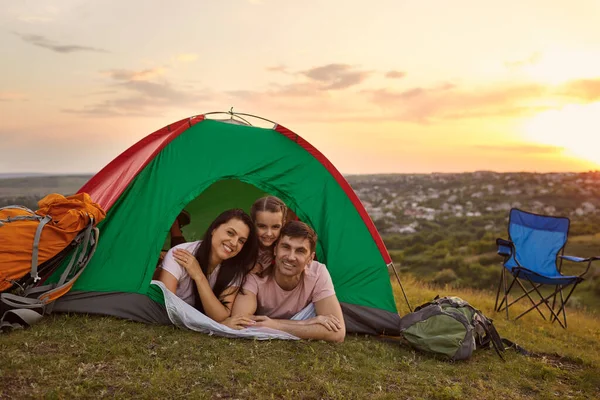 Счастливая семья с ребенком на кемпинге, расслабляясь в палатке. Заботливые родители и их дочь отдыхают в лагере — стоковое фото