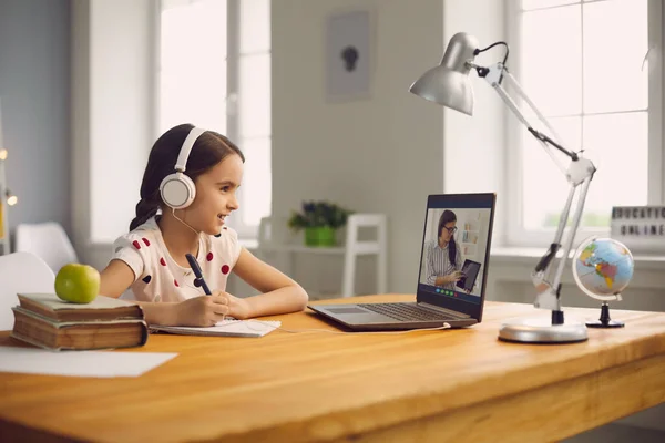 Educación de estudiantes en línea. Colegiala escucha una conferencia de un profesor usando una videoconferencia portátil sentada en una mesa en casa . —  Fotos de Stock