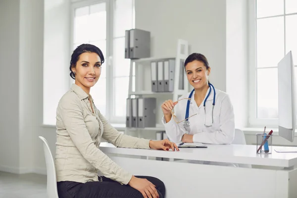 Paciente femenina sonriente en consulta con una doctora sentada en la mesa de la clínica del consultorio . —  Fotos de Stock