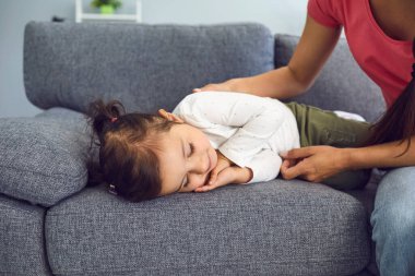 Genç anne, evdeki kanepede uyuyan tatlı kızının yanında. Ebeveyn, güzel çocuğun gündüz uykusuna yatışını izliyor.