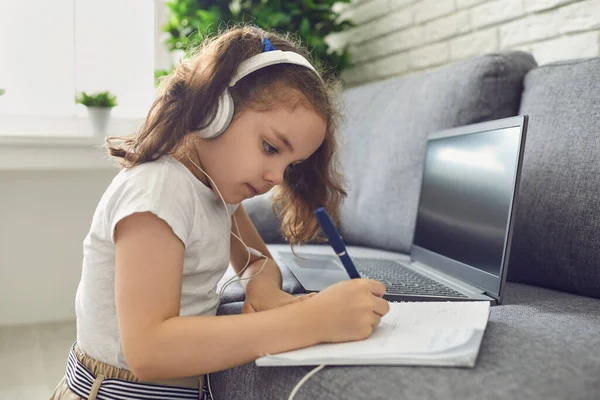 Online education. Video lesson school for children. Little girl child writes in a notebook a lesson in the form of a conference with a teacher at home — Stock Photo, Image