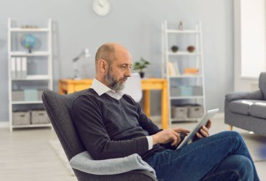 Tabletli kıdemli adam internette mesaj yazıyor, ailesiyle sohbet ediyor, doktora danışıyor ya da evde Webinar izliyor.