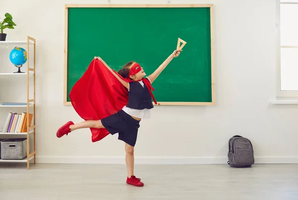 Écolière en costume de super-héros posant sur le fond d'une commission scolaire verte dans une classe d'école. — Photo