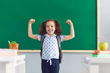 Sınıfta kaslarını gösteren tatlı bir kız. Başarılı olmak için motivasyonunu ifade eden güçlü bir çocuk. Okula geri dön.