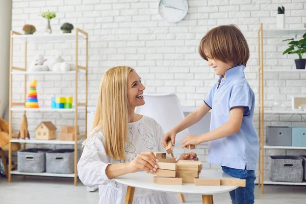 Ibu muda yang cantik bermain papan permainan dengan anaknya di rumah. Induk dan anak membangun menara dari balok kayu — Stok Foto
