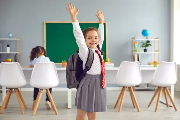 Концепція повернення до школи. Щаслива школярка посміхається підняв руки вгору, стоячи в класі . — стокове фото