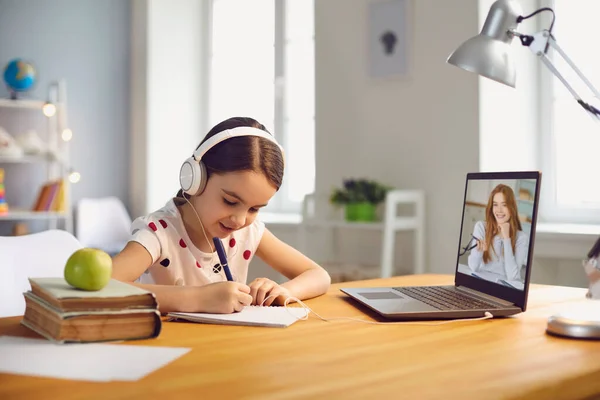 Schulmädchen lernen online. Mädchen in lässiger Kleidung sieht Videochat Lehrer Vorlesung hat Laptop am Tisch zu Hause sitzen — Stockfoto