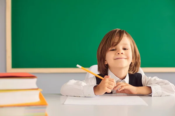 Повернутися до школи. Симпатичний хлопчик школяр посміхається, сидячи за столом на фоні шкільної дошки . — стокове фото