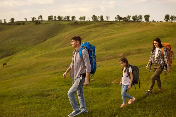 Família feliz com criança mochila nas montanhas. Mãe, pai e filha caminhadas no campo no dia de verão — Fotografia de Stock