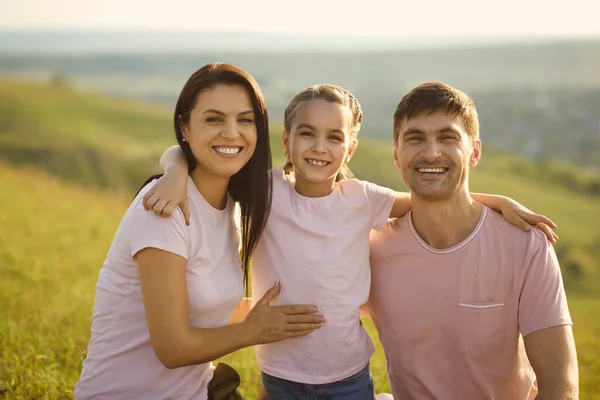 Portret van positieve jonge familie kijkend naar camera op het platteland. schattig meisje knuffelen haar ouders op zomer vakantie — Stockfoto