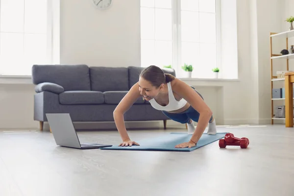 Bella ragazza in forma in abbigliamento sportivo guardando video di allenamento online e facendo flessioni o esercizio tavola a casa — Foto Stock