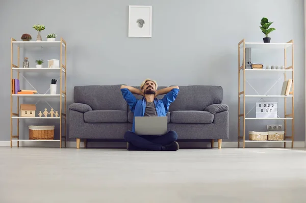 Uomo d'affari soddisfatto in abiti casual con un computer portatile sogna seduto sul pavimento in soggiorno. — Foto Stock