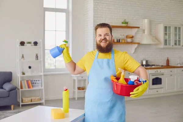 Hombre gordo divertido en un delantal y guantes de limpieza amarillos está limpiando en la habitación . — Foto de Stock